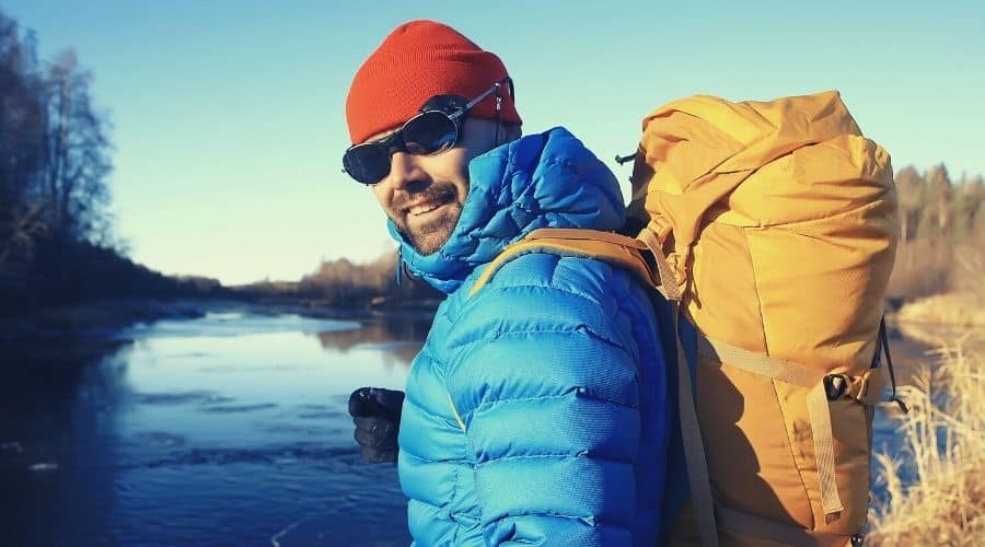 hiker wearing ski goggles down jacket next to lake