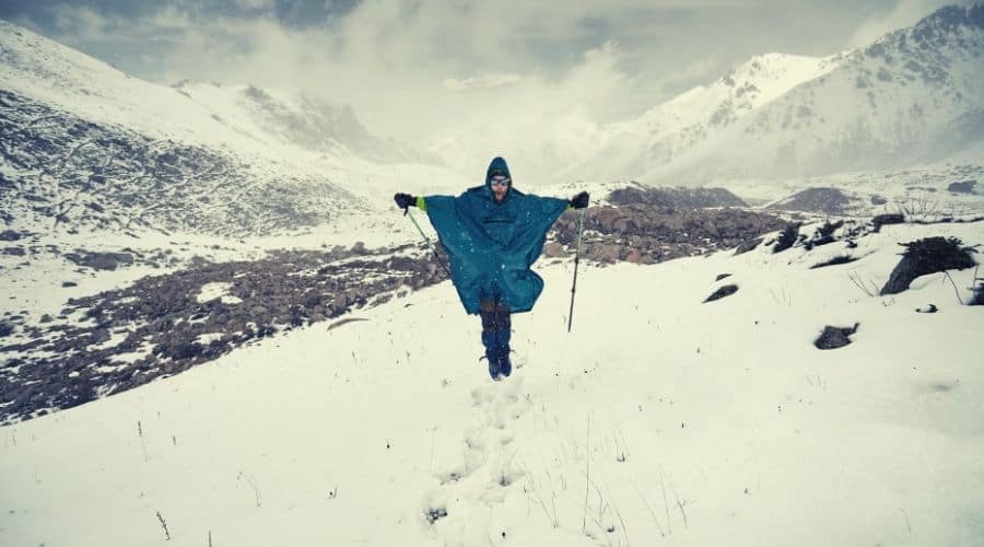hiker with poles and poncho hiking in deep snow through valley