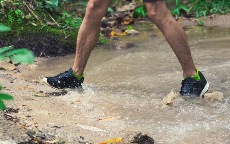 Man wearing trail runners walking through a large puddle