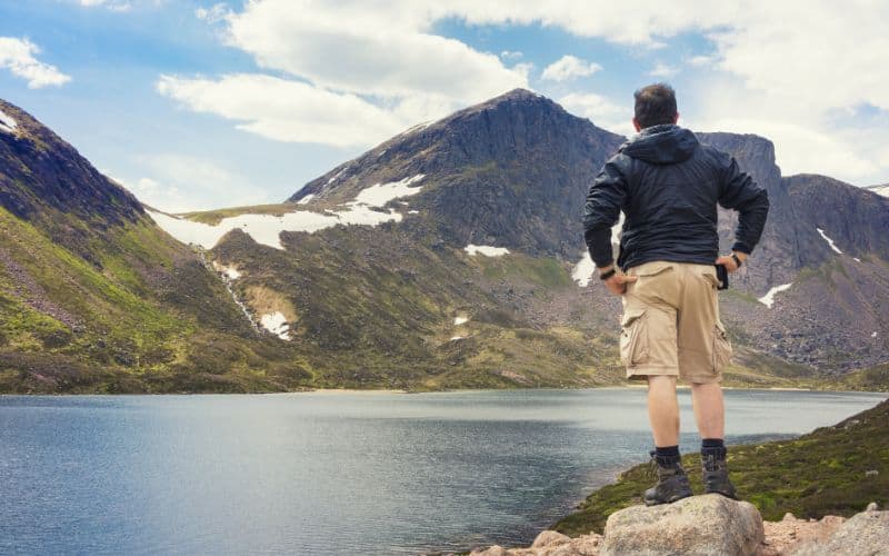 Hiker wearing cargo shorts with large pockets standing in front of mountains and a lake