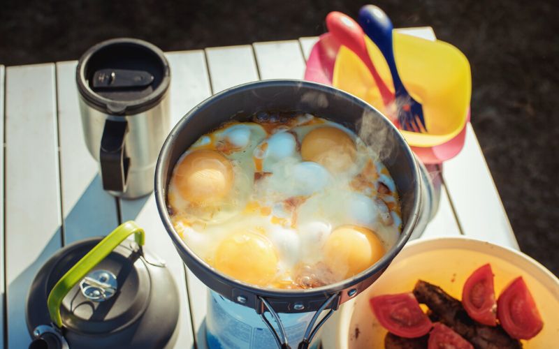 Eggs frying on camp stove along with other camp kitchen accessories