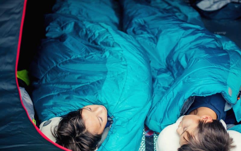 Two kids sleeping in sleeping bags in tent