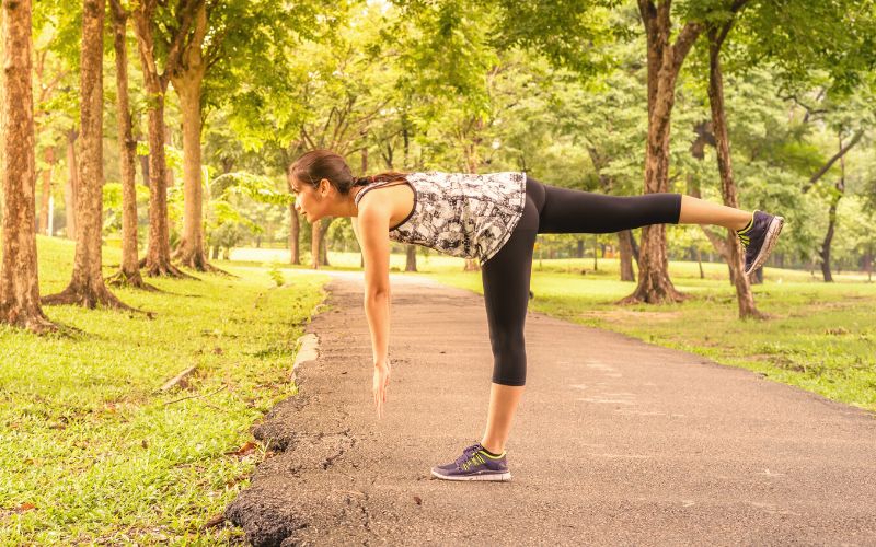 Woman in park doing stretches on one leg