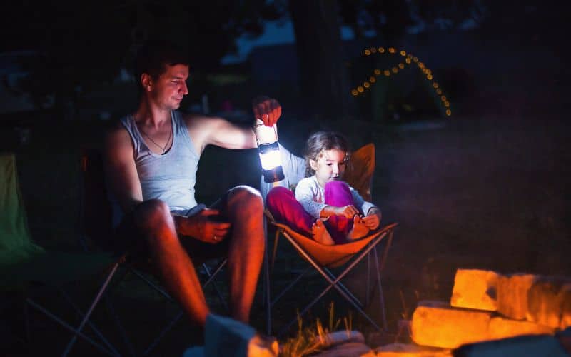 Father sitting with child sitting on camp chairs and holding a lantern